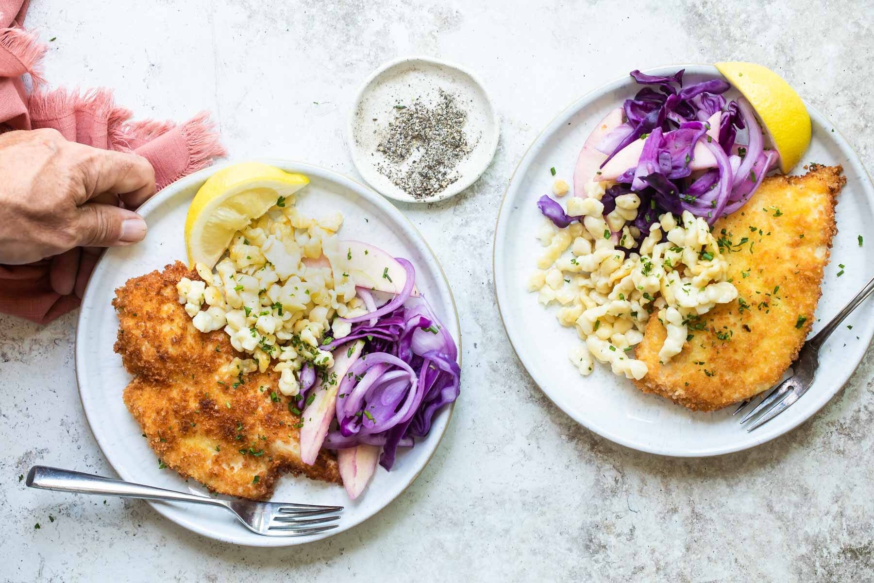 2 plates with chicken schnitzel, spatzle, and braised red cabbage.
