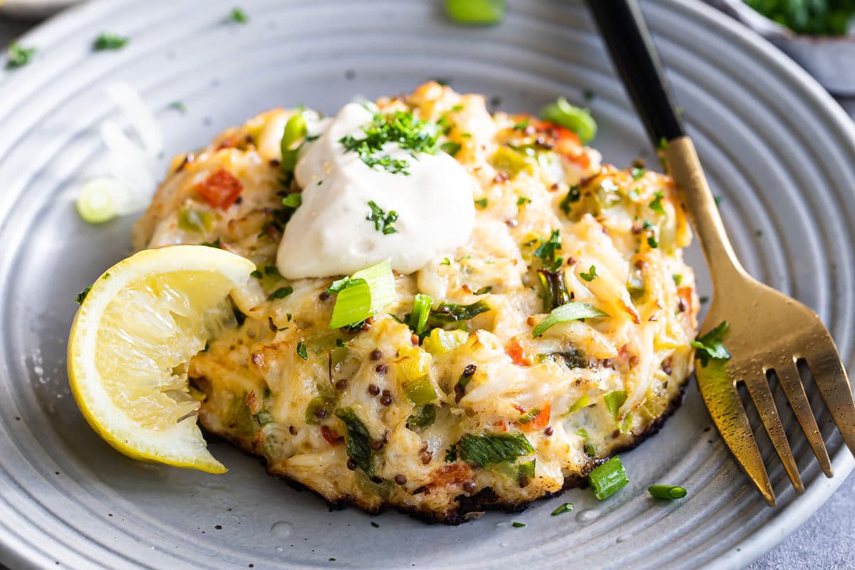 A crab cake on gray plate with a lemon wedge garnish.