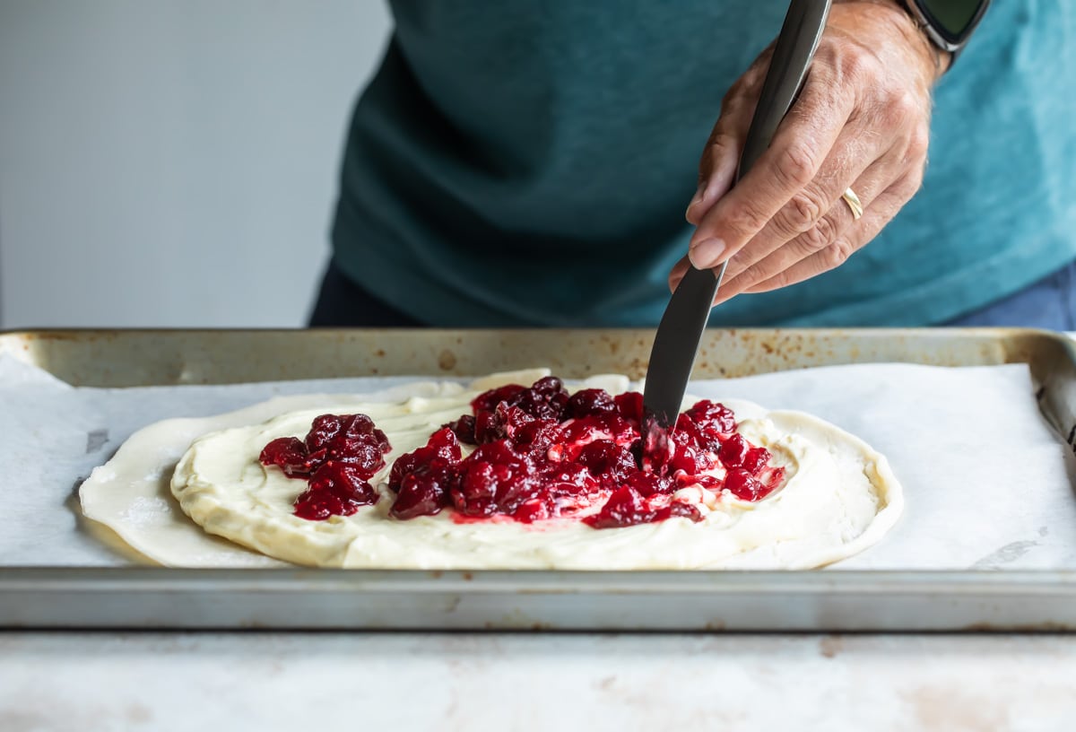 Someone spreading cranberries on dough to make a cranberry cheesecake galette.
