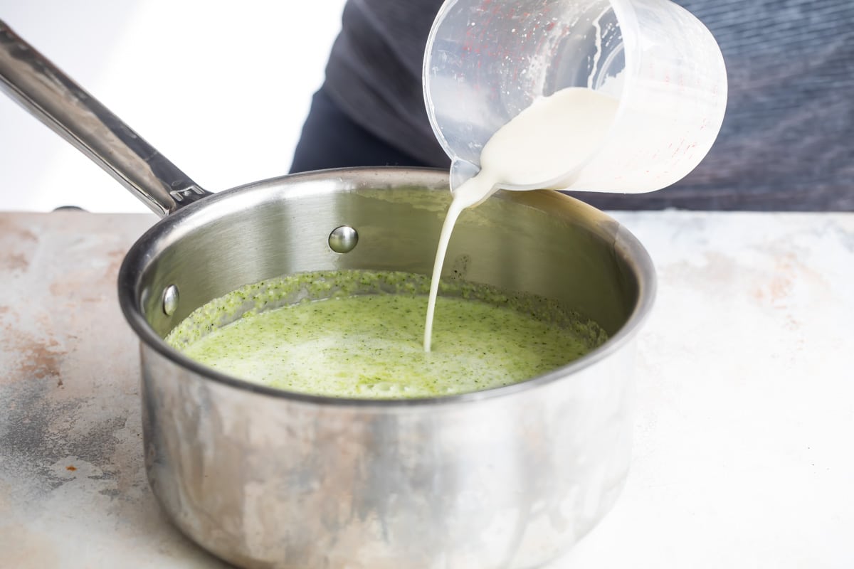 Someone adding cream to cream of broccoli soup.