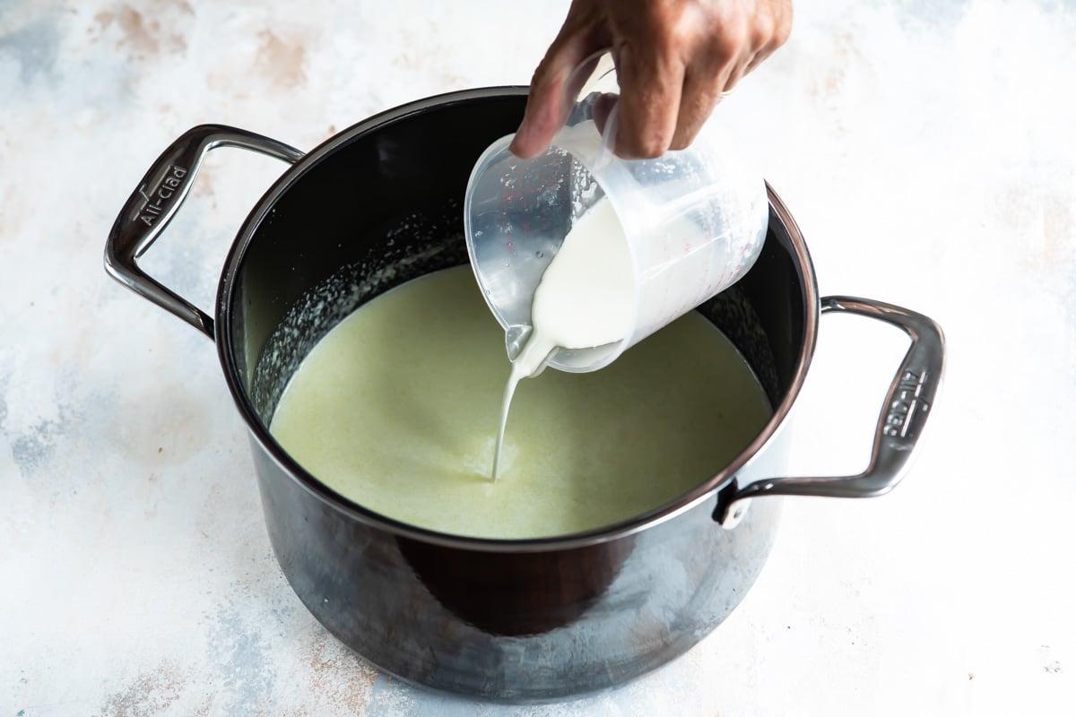Someone adding cream to a pot with green liquid.