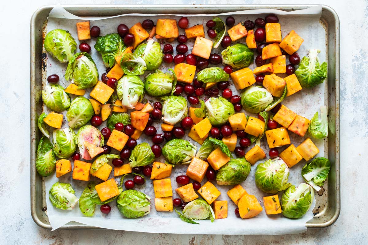 Uncooked harvest roasted vegetables on a parchment paper lined sheet pan.