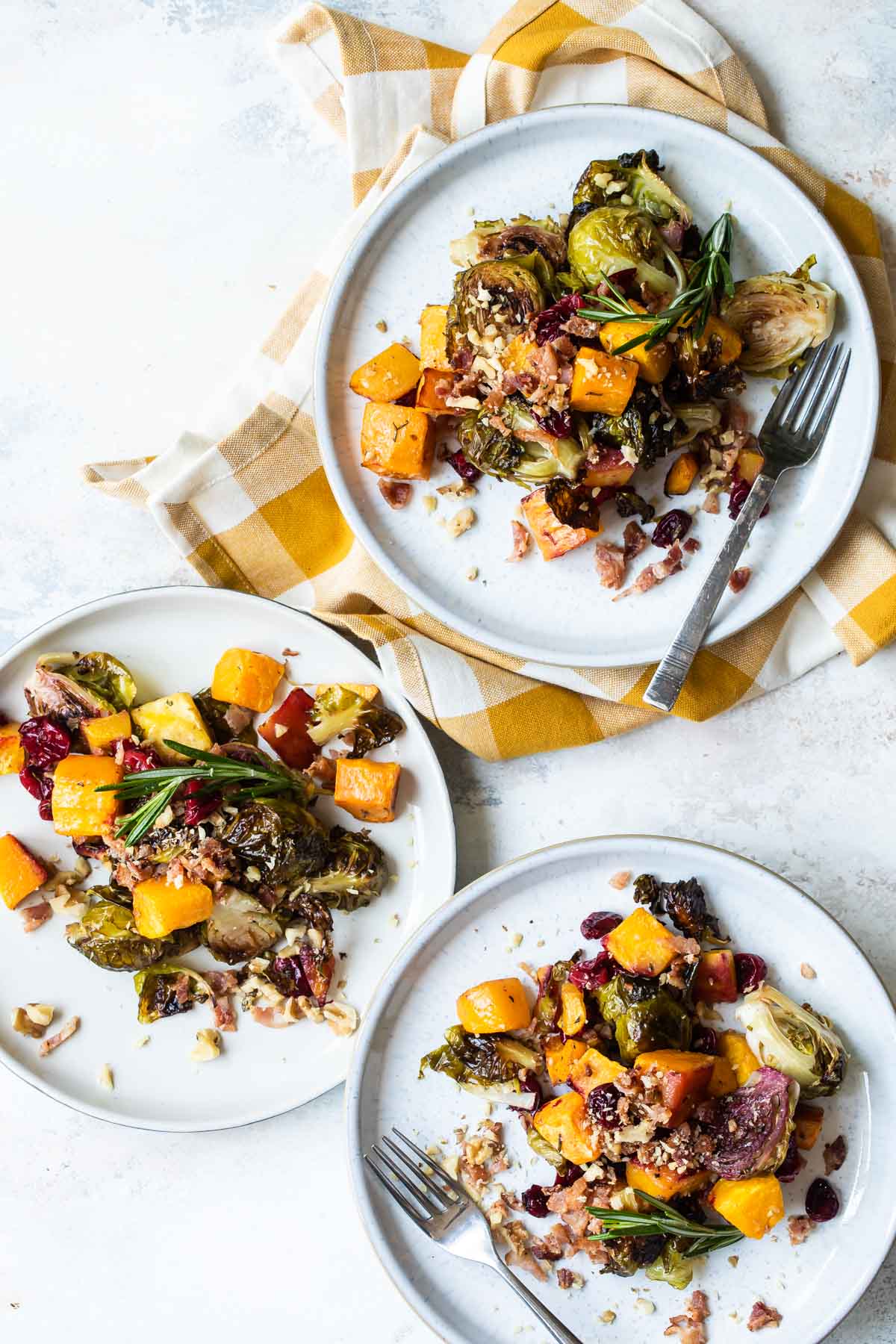 Three servings of harvest roasted vegetables on separate white plates.