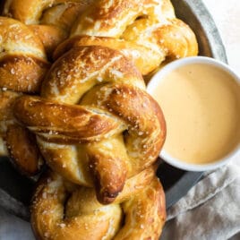 A platter of soft pretzels with a bowl of cheese sauce.