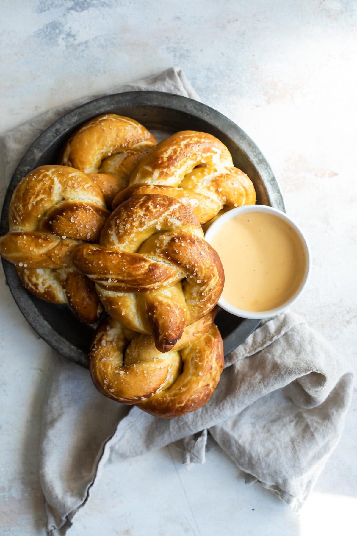 A platter of soft pretzels with a bowl of cheese sauce.