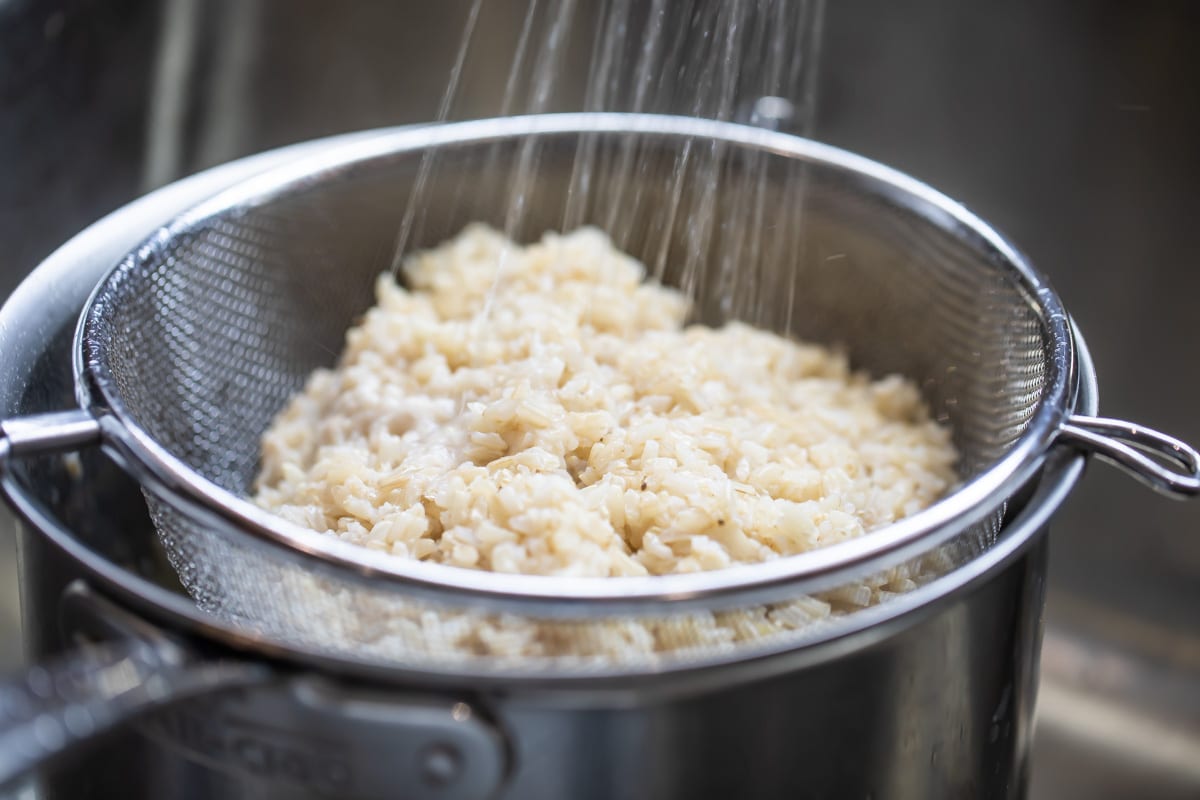 Someone rinsing brown rice in a mesh strainer.