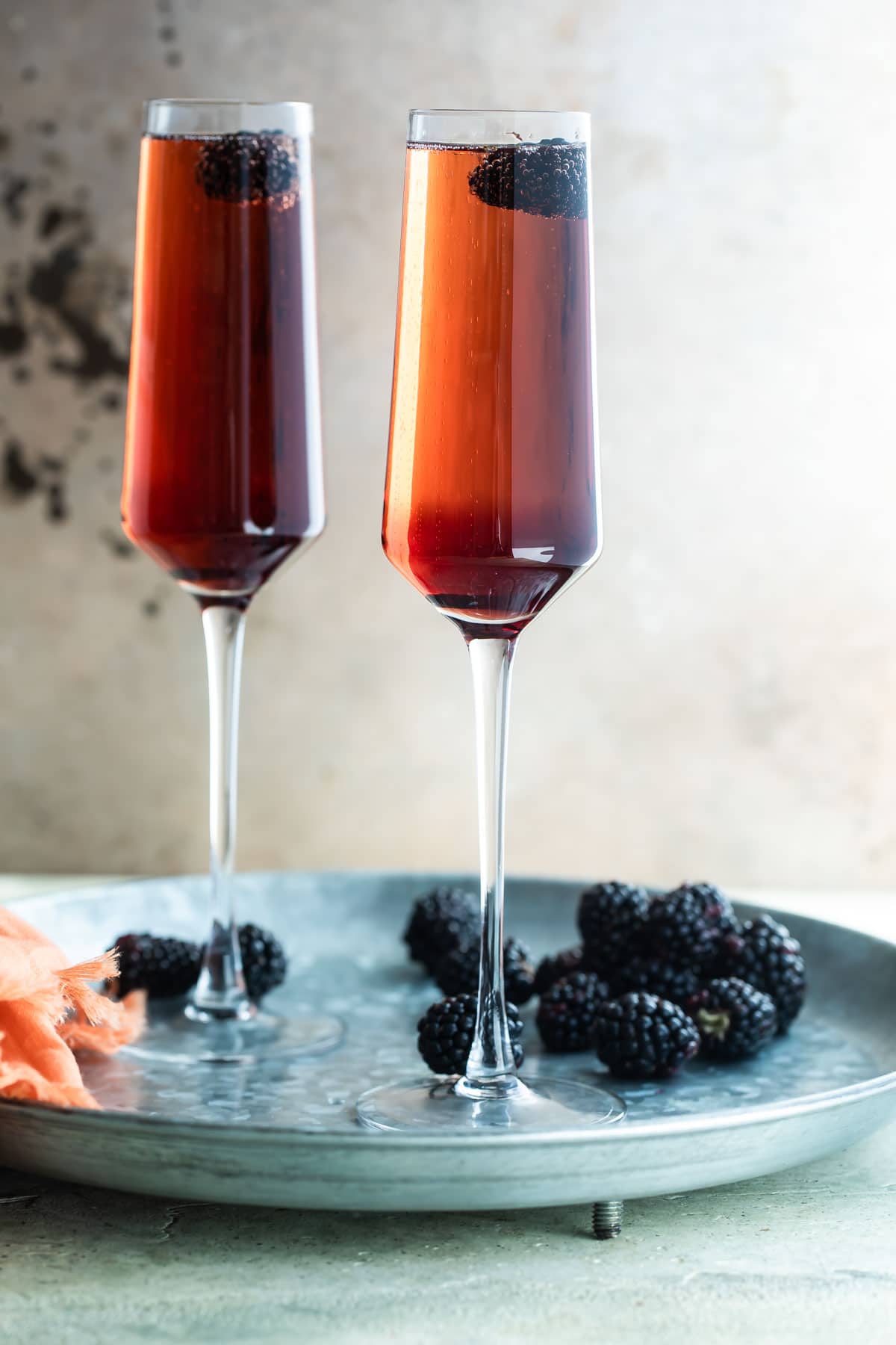 Two Kir Royale cocktails in champagne flutes on a metal tray.