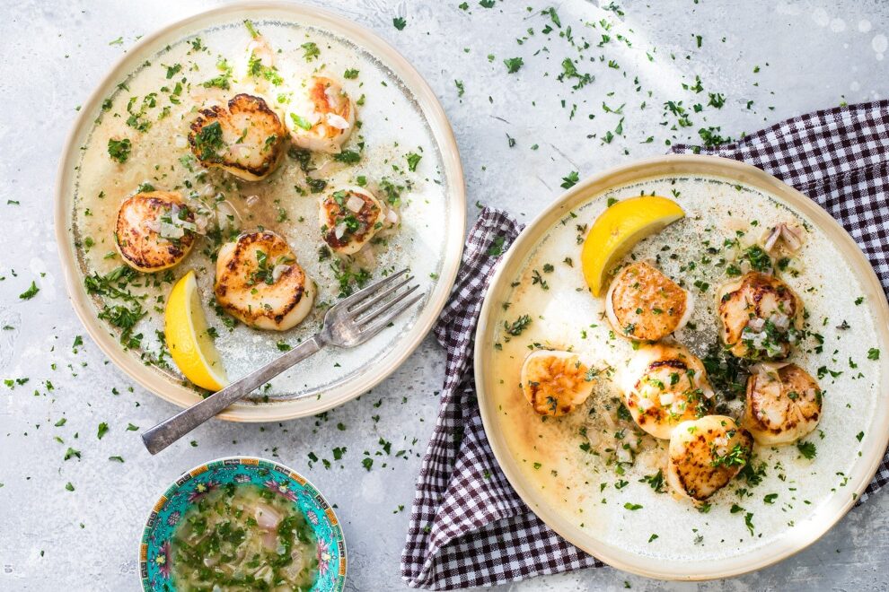 Two plates with pan-seared scallops and lemon butter.