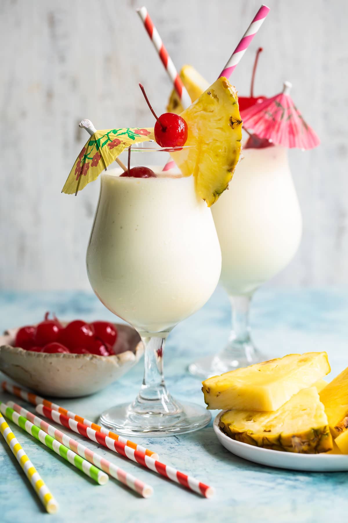 Two piña coladas garnished with pineapple and cherries.
