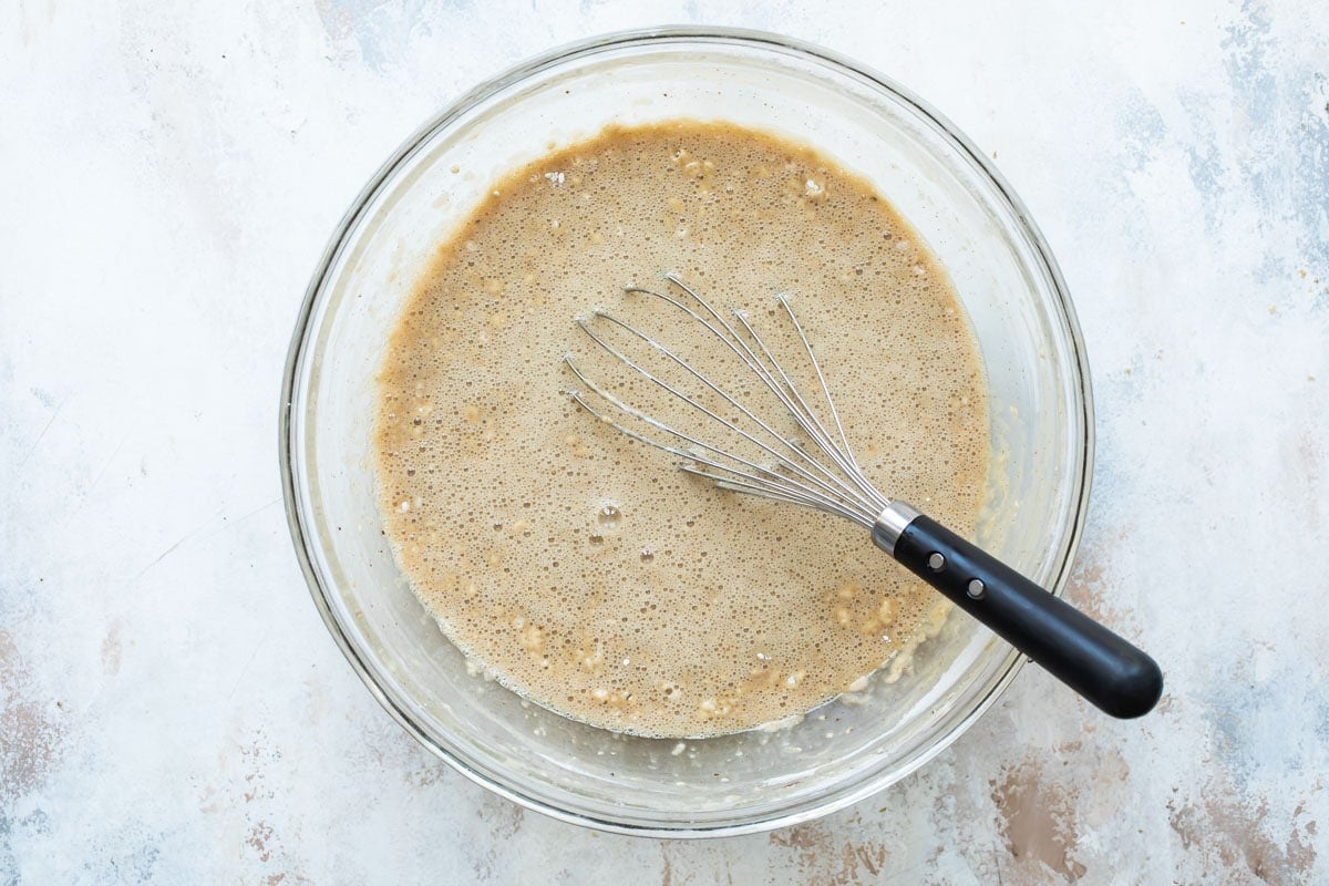 Spice cake batter in a clear mixing bowl with a whisk resting in it.