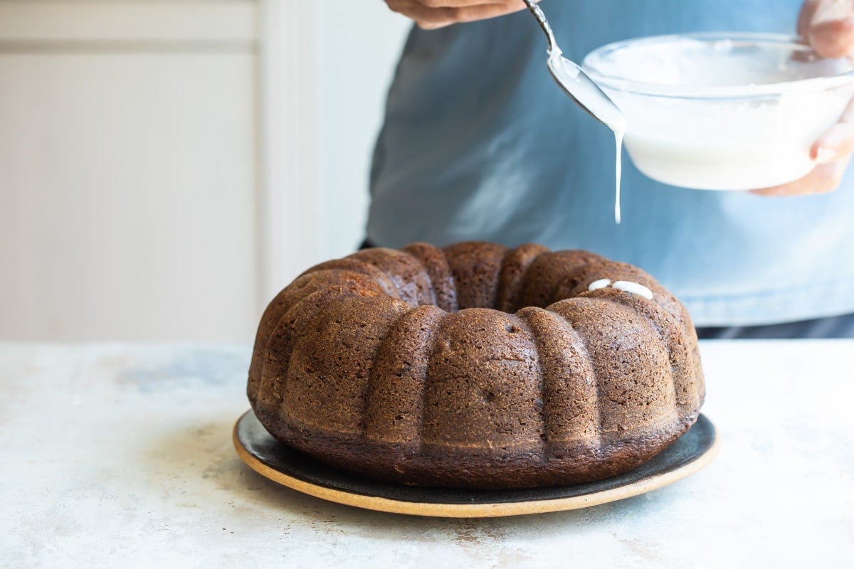 Someone drizzling icing on a round spice cake.