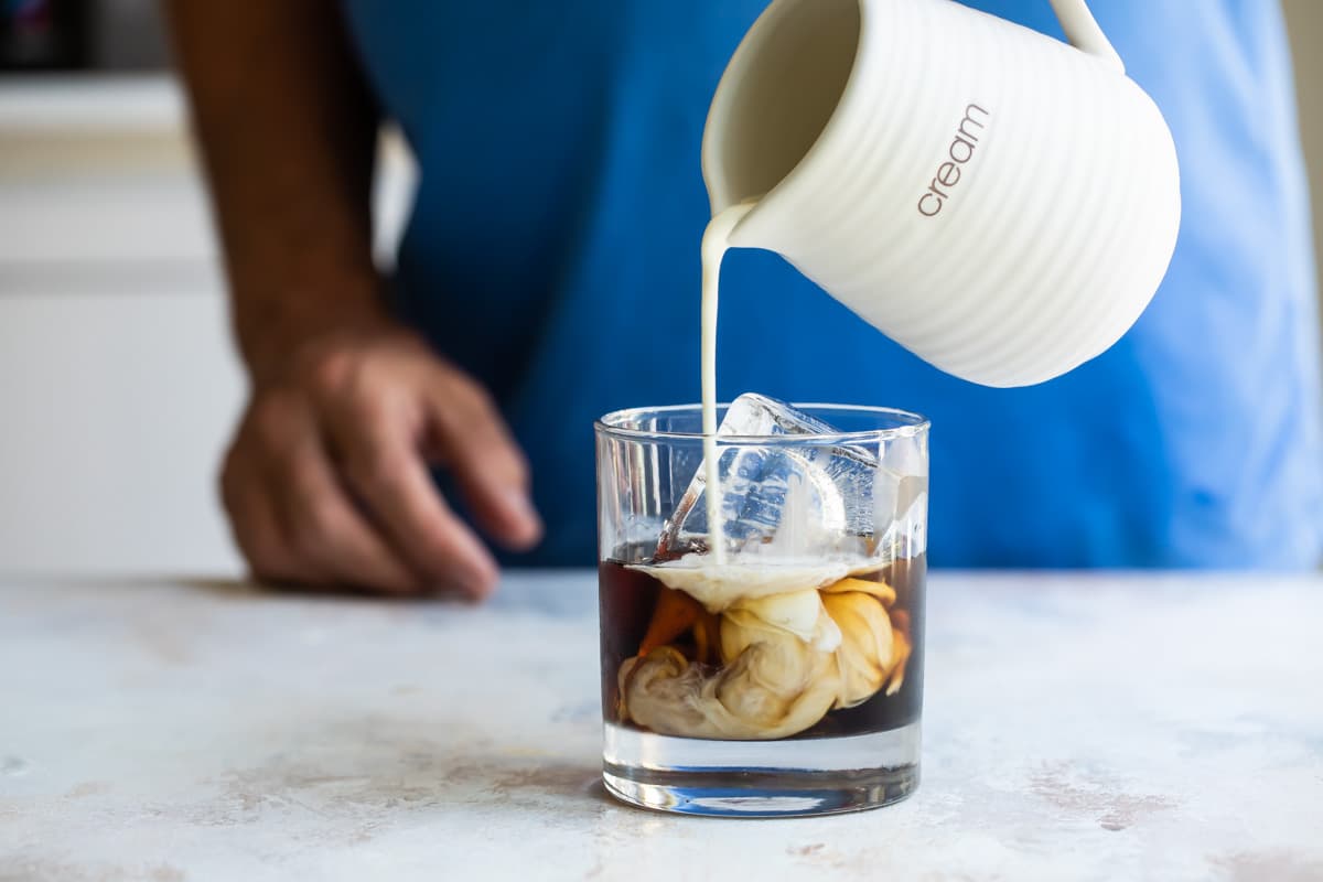 Someone pouring cream into a glass of Kahlua and vodka to make a white Russian.