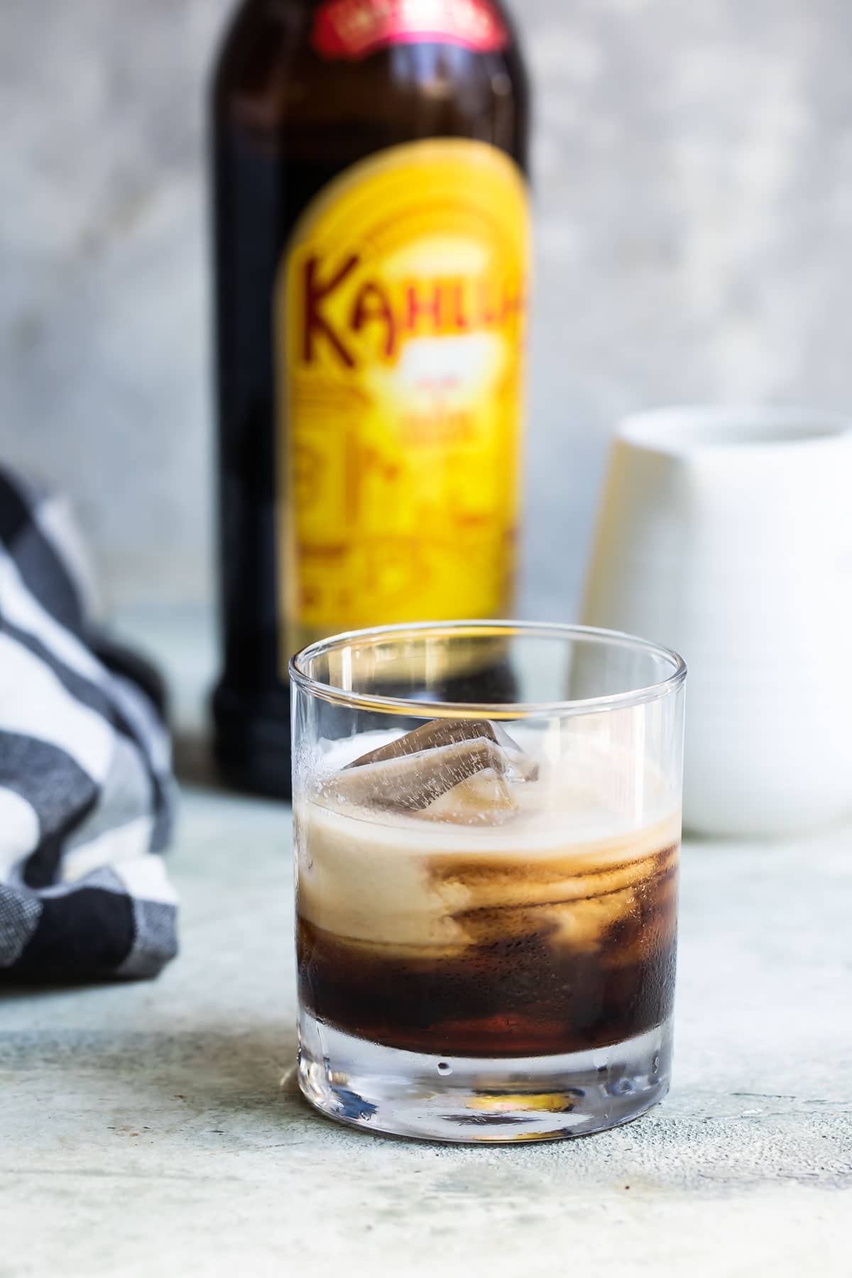 A white Russian cocktail with a bottle of Kahlua in the background.