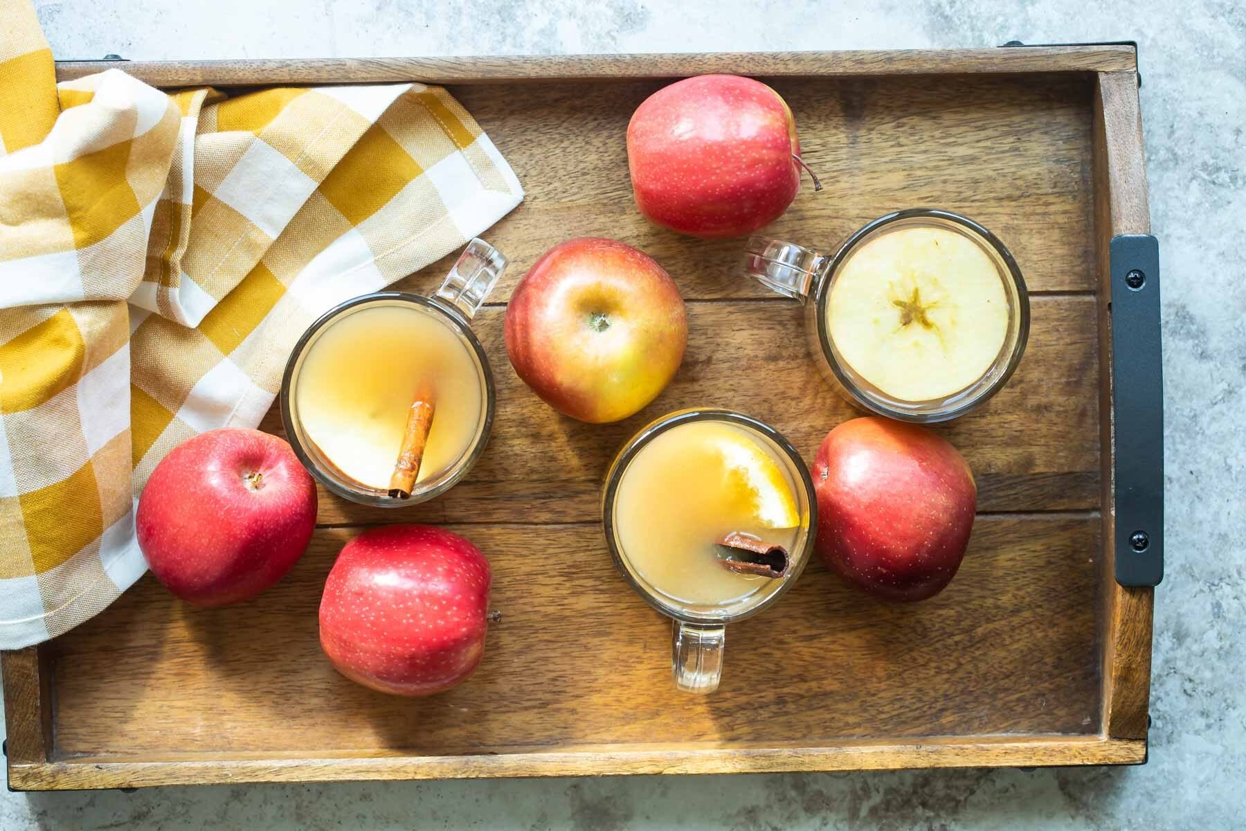Apple cider in a clear glasses on a wooden serving tray.