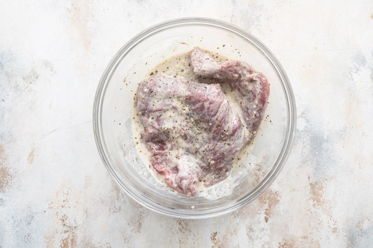 Large pieces of beef marinating in tzatziki sauce in a bowl.