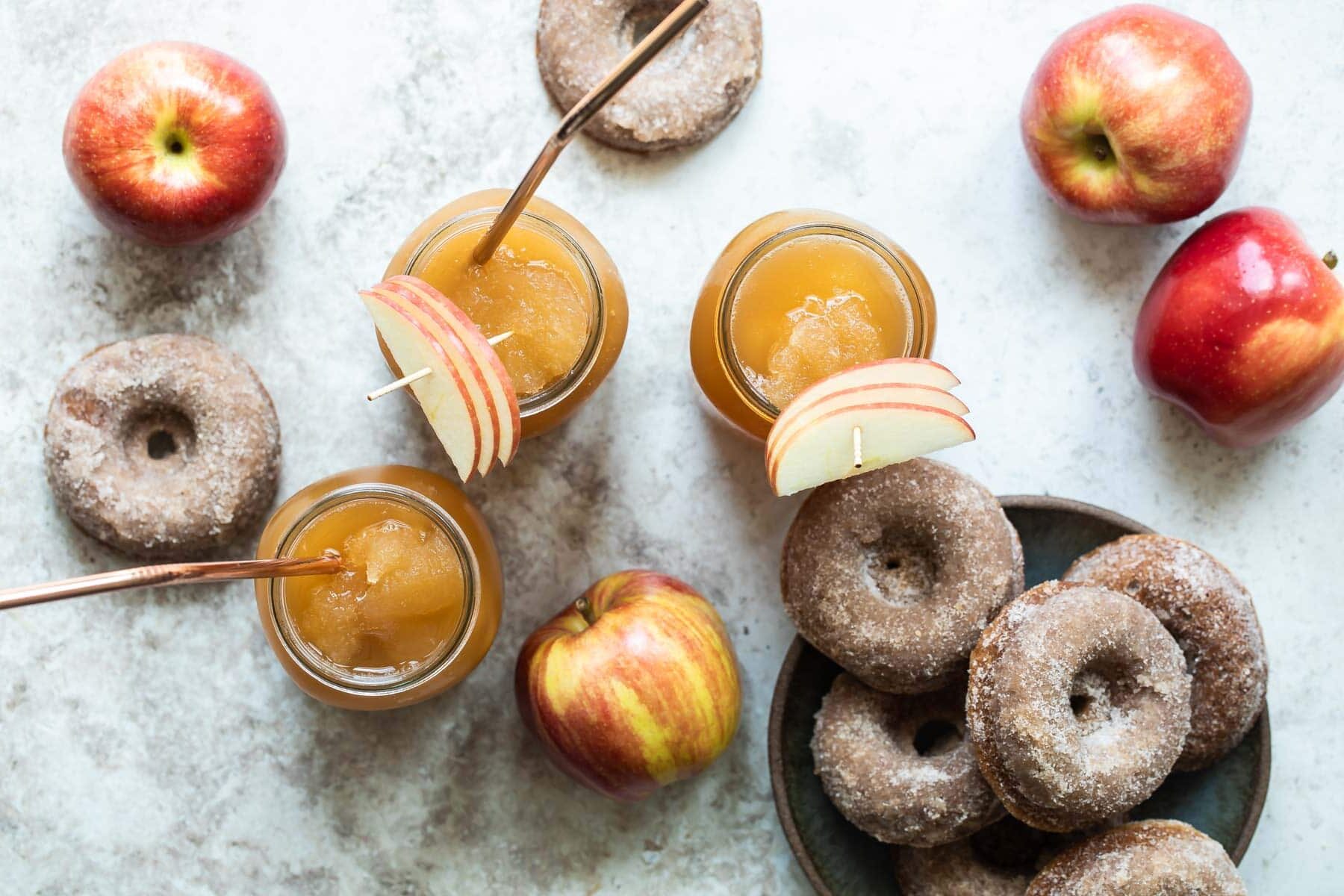 Three mason jars of brandy apple cider slush surrounded by donuts and apples.