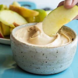 An apple being dipped in caramel apple dip.