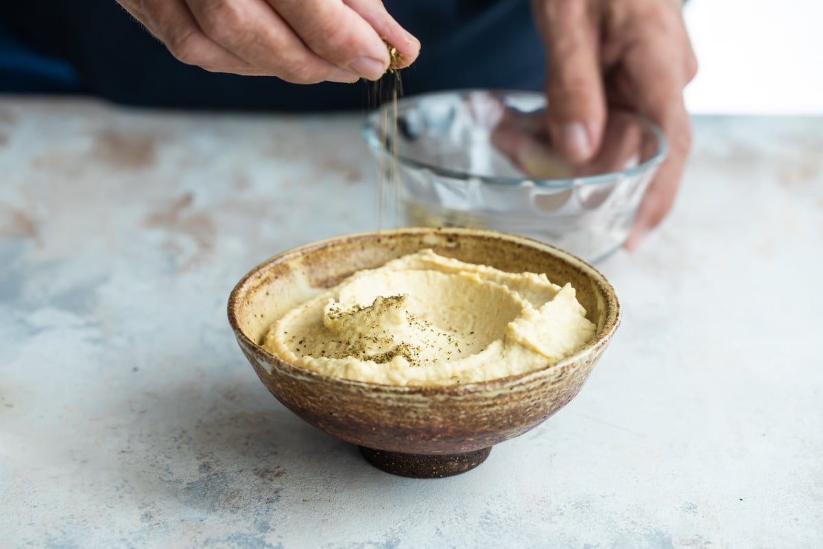 Someone sprinkling seasoning onto homemade hummus.