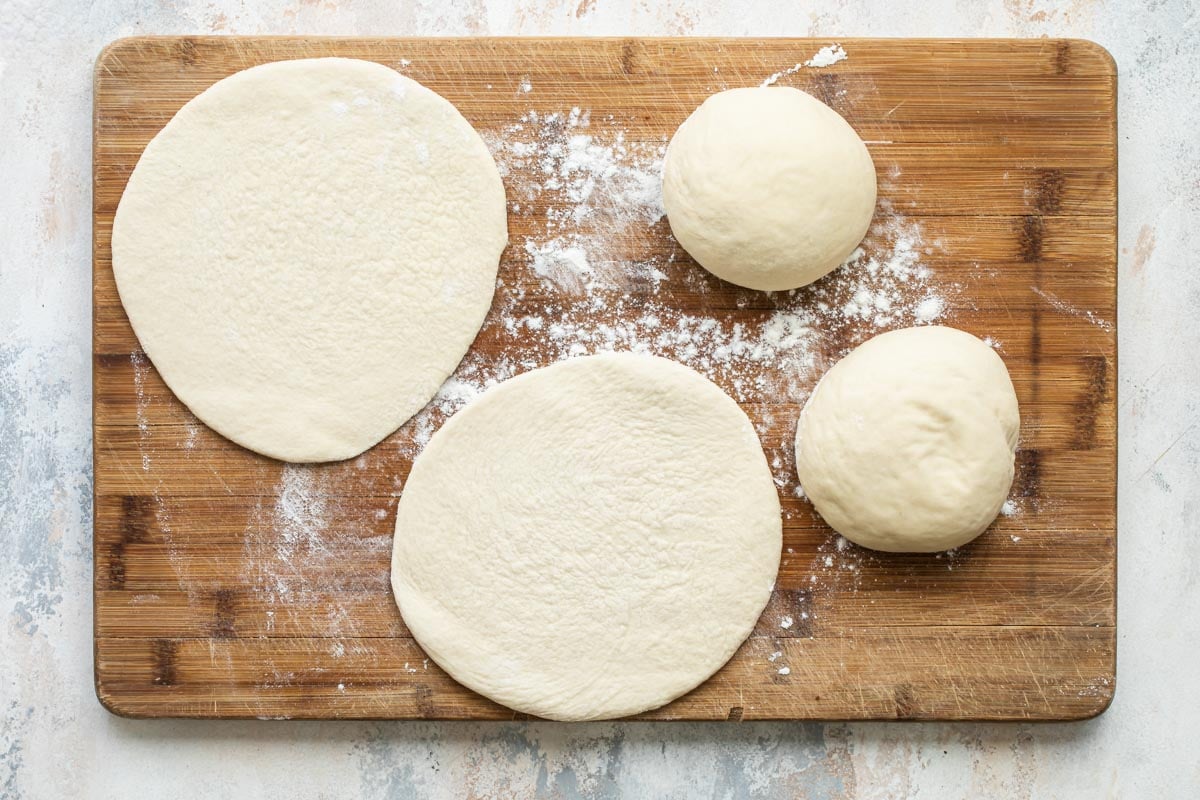 Homemade pita bread dough flattened and in balls on a cutting board.