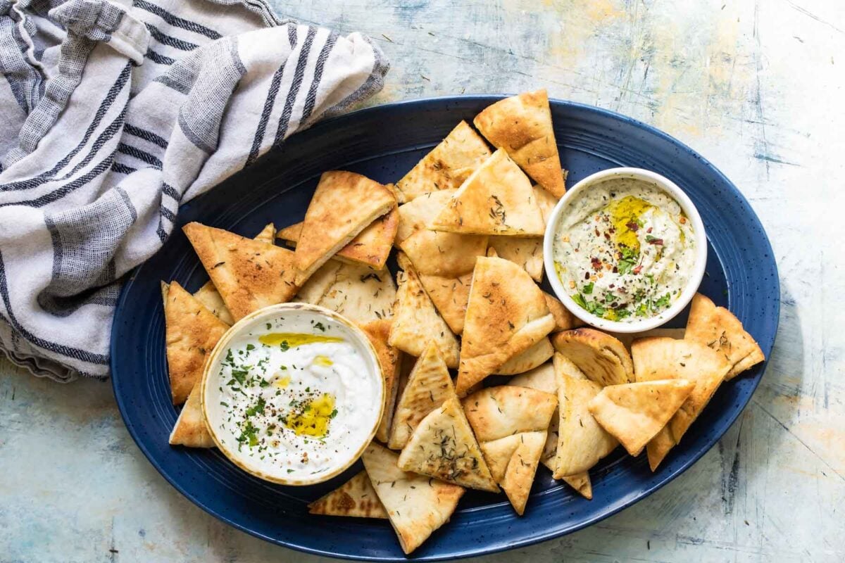 Homemade pita chips on a platter with bowls of hummus.