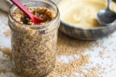 A mason jar with mustard and a red spoon in it.