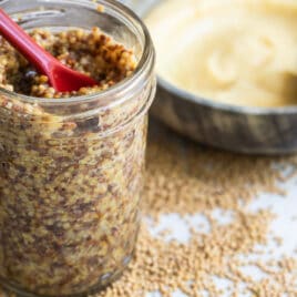 A mason jar with mustard and a red spoon in it.