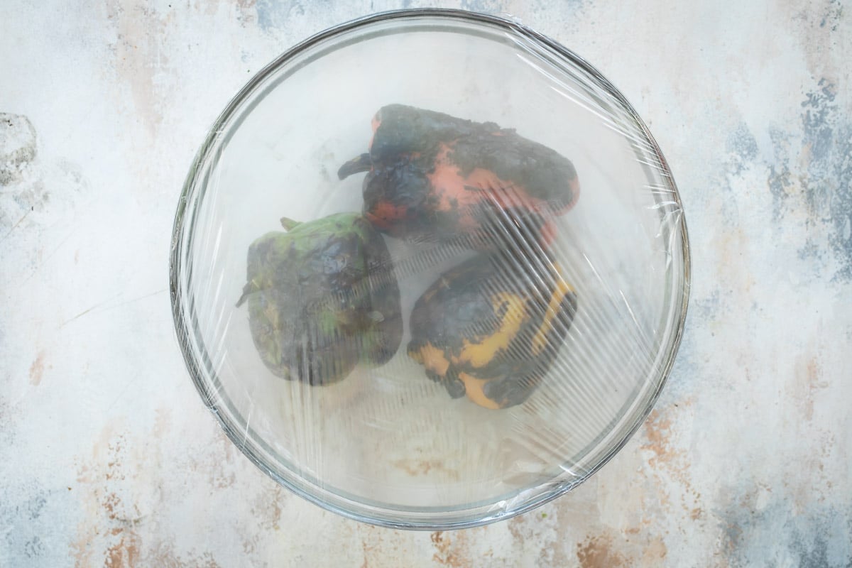 Roasted peppers in a glass bowl covered with cling wrap.
