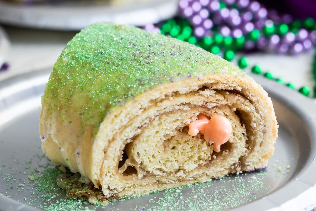 A slice of king cake with a plastic baby popping out on a silver plate.