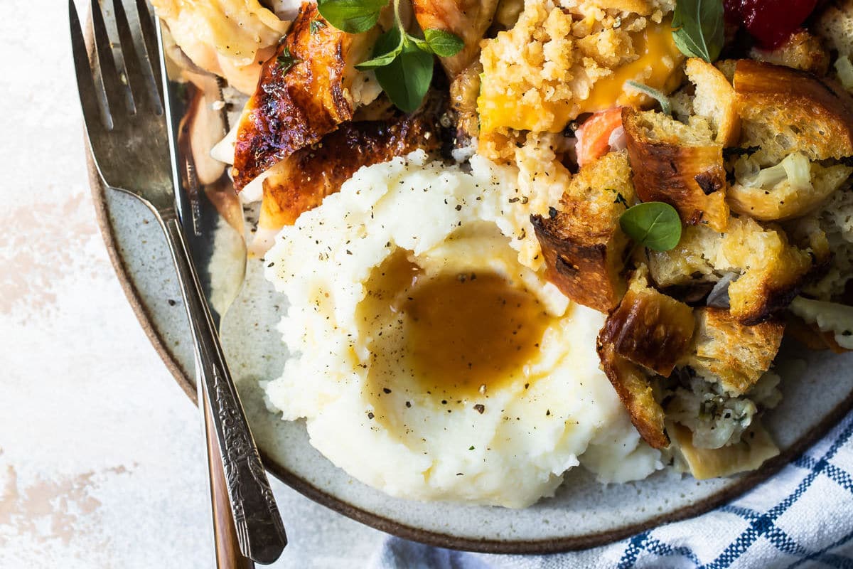 A plate of roasted cornish hen, mashed potatoes, stuffing, vegetable casserole, and cranberry sauce.