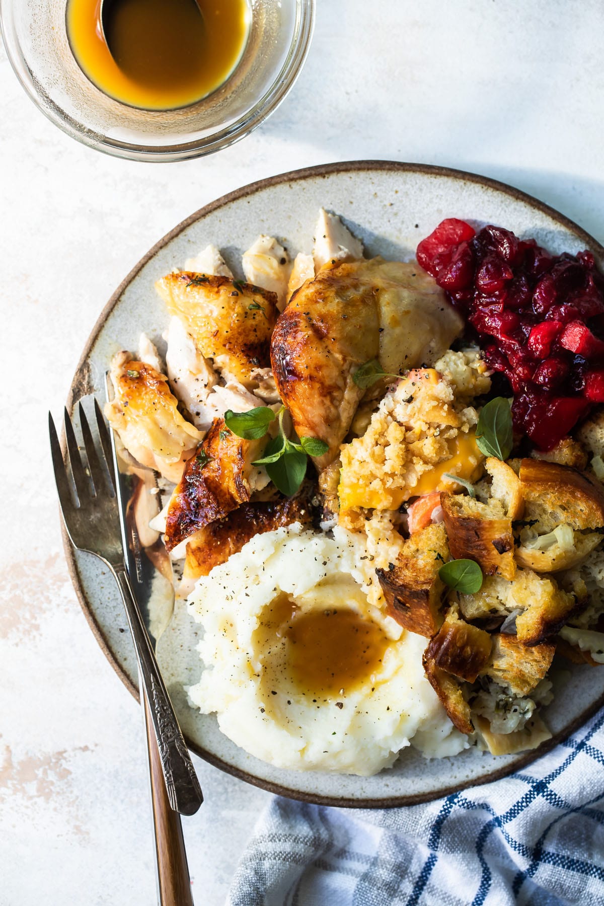 A plate of roasted cornish hen, mashed potatoes, stuffing, vegetable casserole, and cranberry sauce.