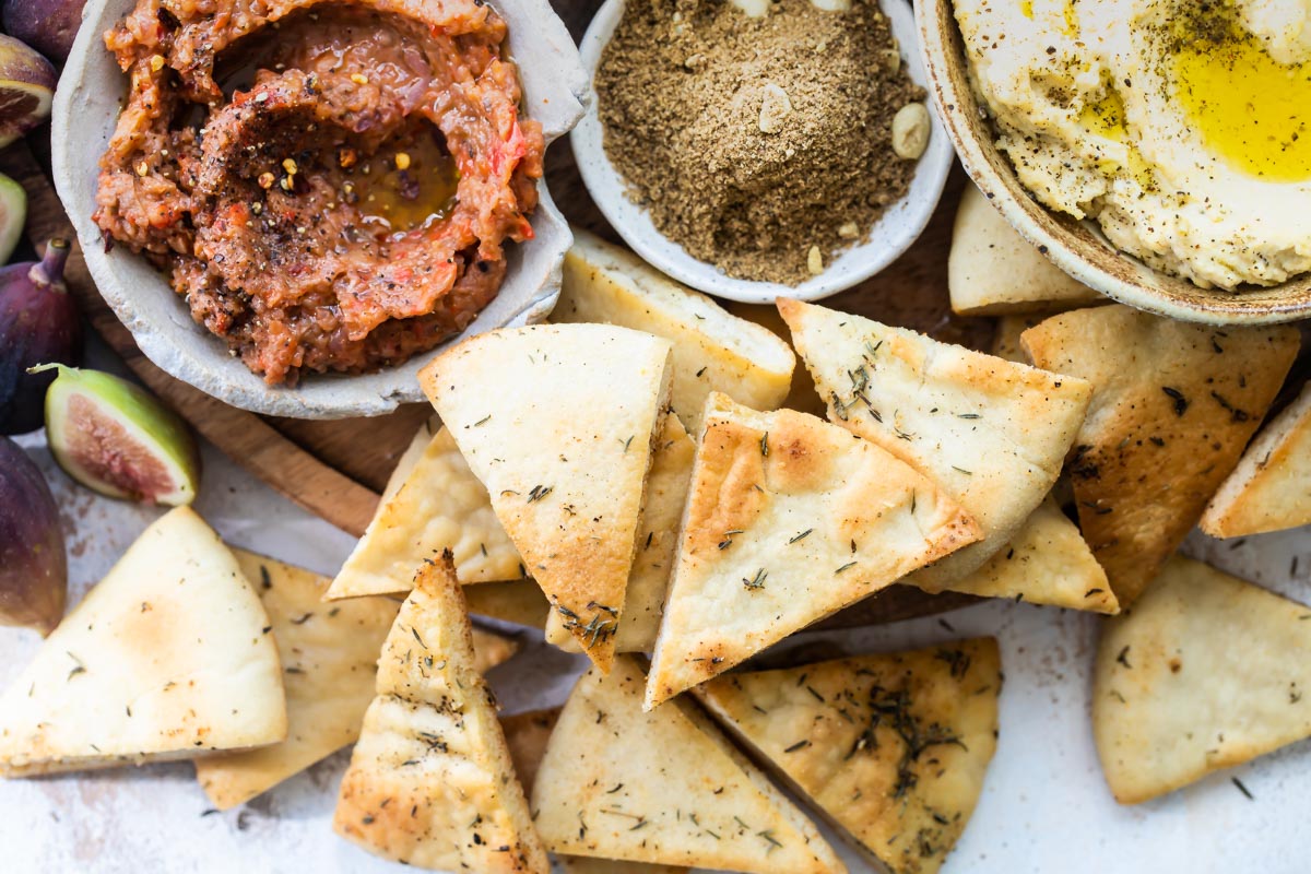 Eggplant dip and hummus in bowls surrounded by pita bread.