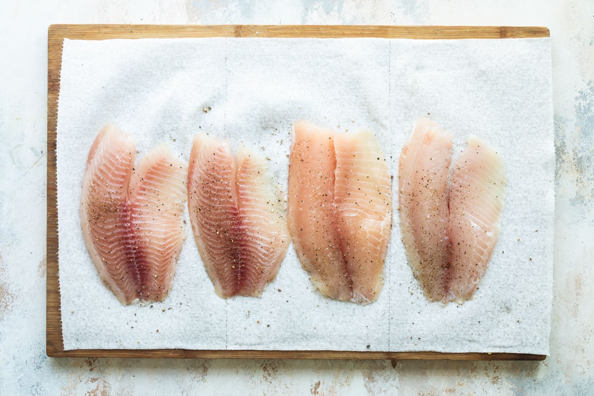 4 pieces of seasoned tilapia on a cutting board.