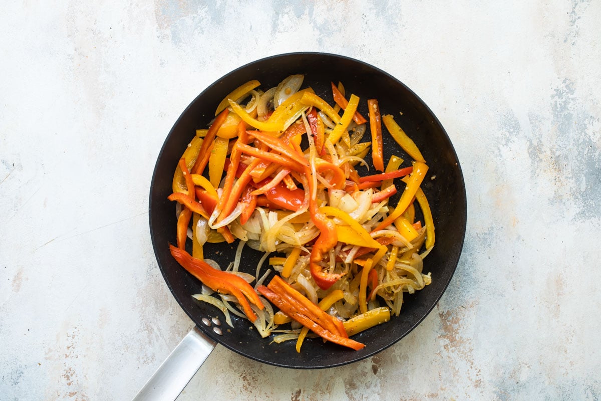 Sliced peppers and onions in a skillet.