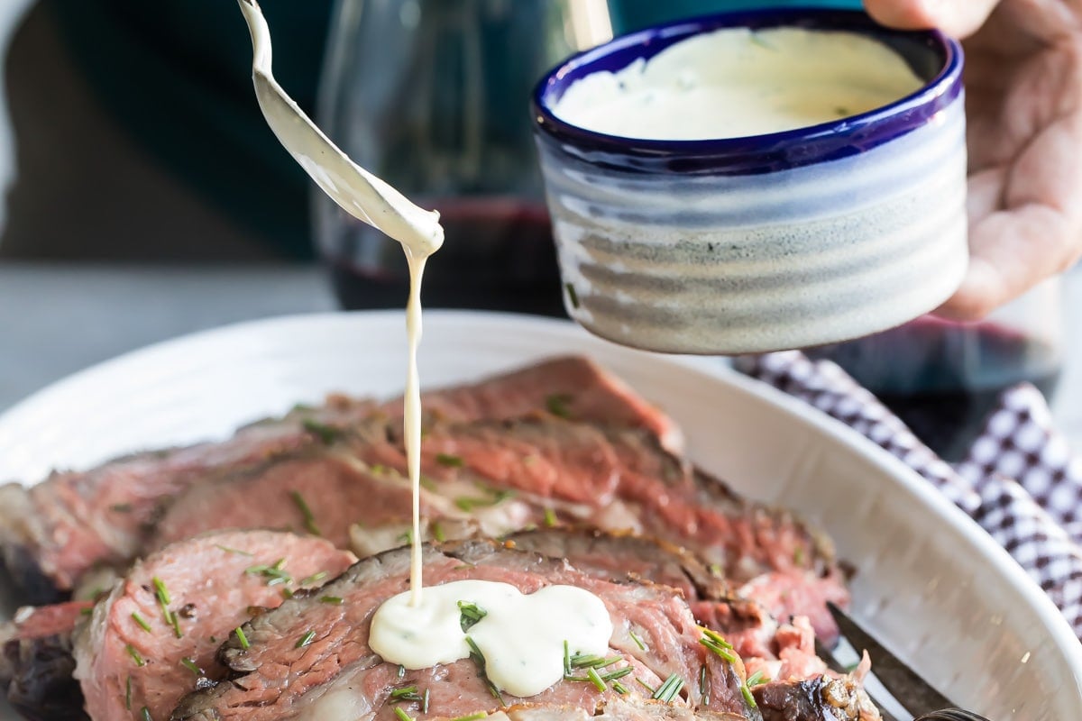 Drizzling mustard cream sauce on sliced prime rib.