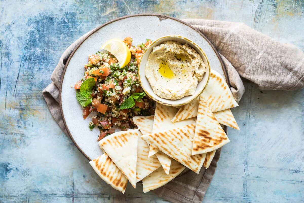 Quinoa tabbouleh on a plate with a side of hummus and pita triangles.