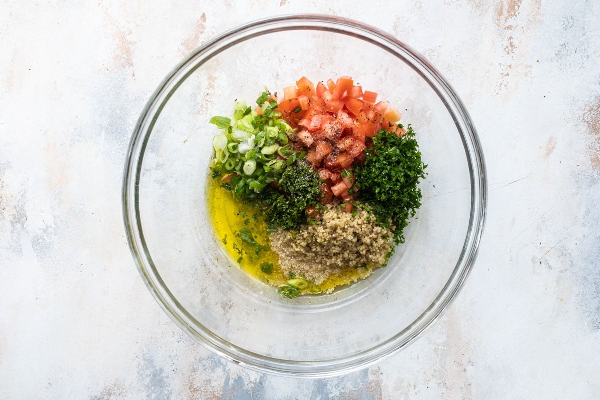 Ingredients of quinoa tabbouleh pre mixed in a clear bowl.