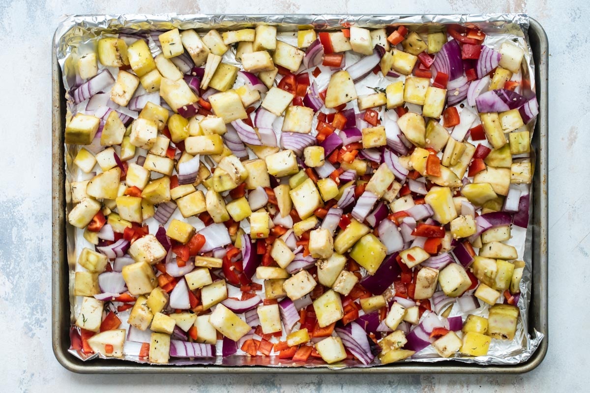 Cubed eggplant and veggies on a baking sheet.