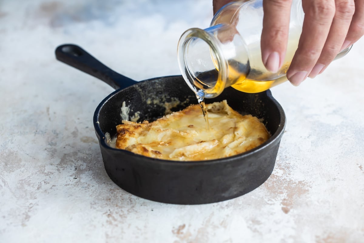 Liquid being poured over Saganaki in a small cast iron pan.