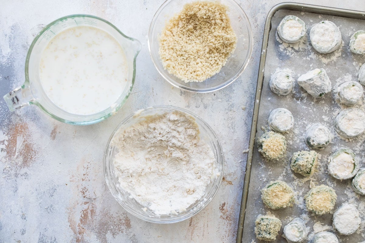 Jalapeño poppers being coated in flour and bread crumbs.
