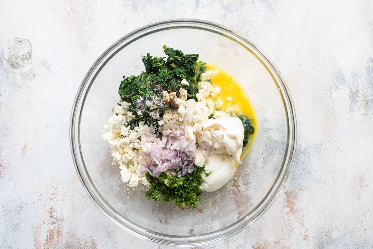 All of the three cheese spanakopita filling ingredients in a clear bowl.
