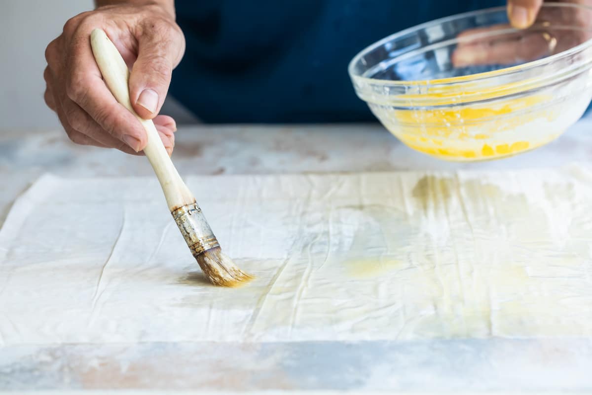 Someone brushing an egg wash onto a sheet of pastry dough.