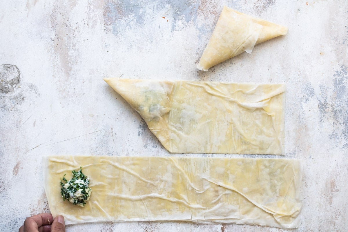 Three steps on how to stuff and fold the spanakopita filling into the pastry slices.