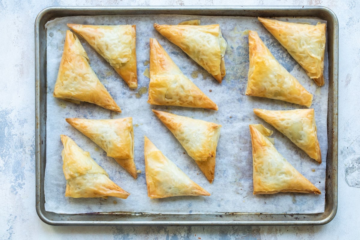 Baked three cheese spanakopita triangles on a baking sheet.