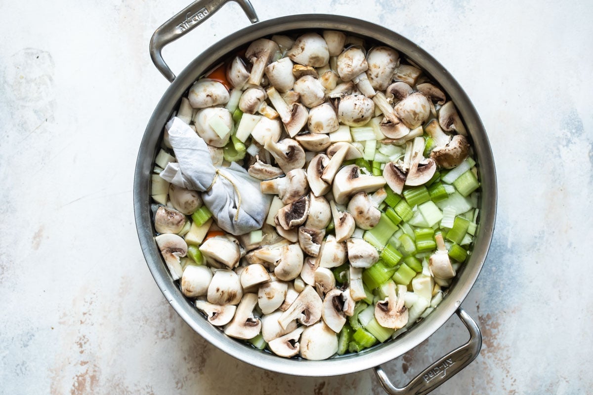 Raw chopped vegetables submerged in water in a silver pot.