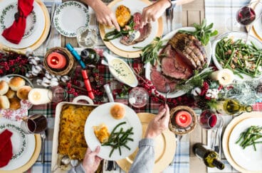 A Christmas table with prime rib, scalloped potatoes, green beans, and rolls.