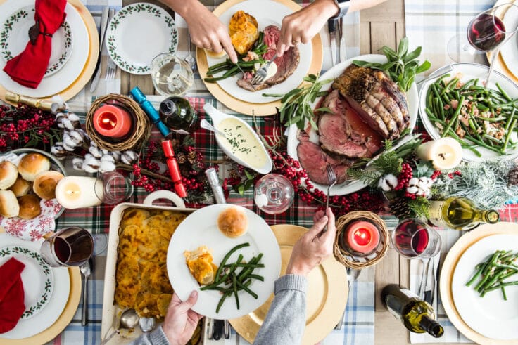 A Christmas table with prime rib, scalloped potatoes, green beans, and rolls.
