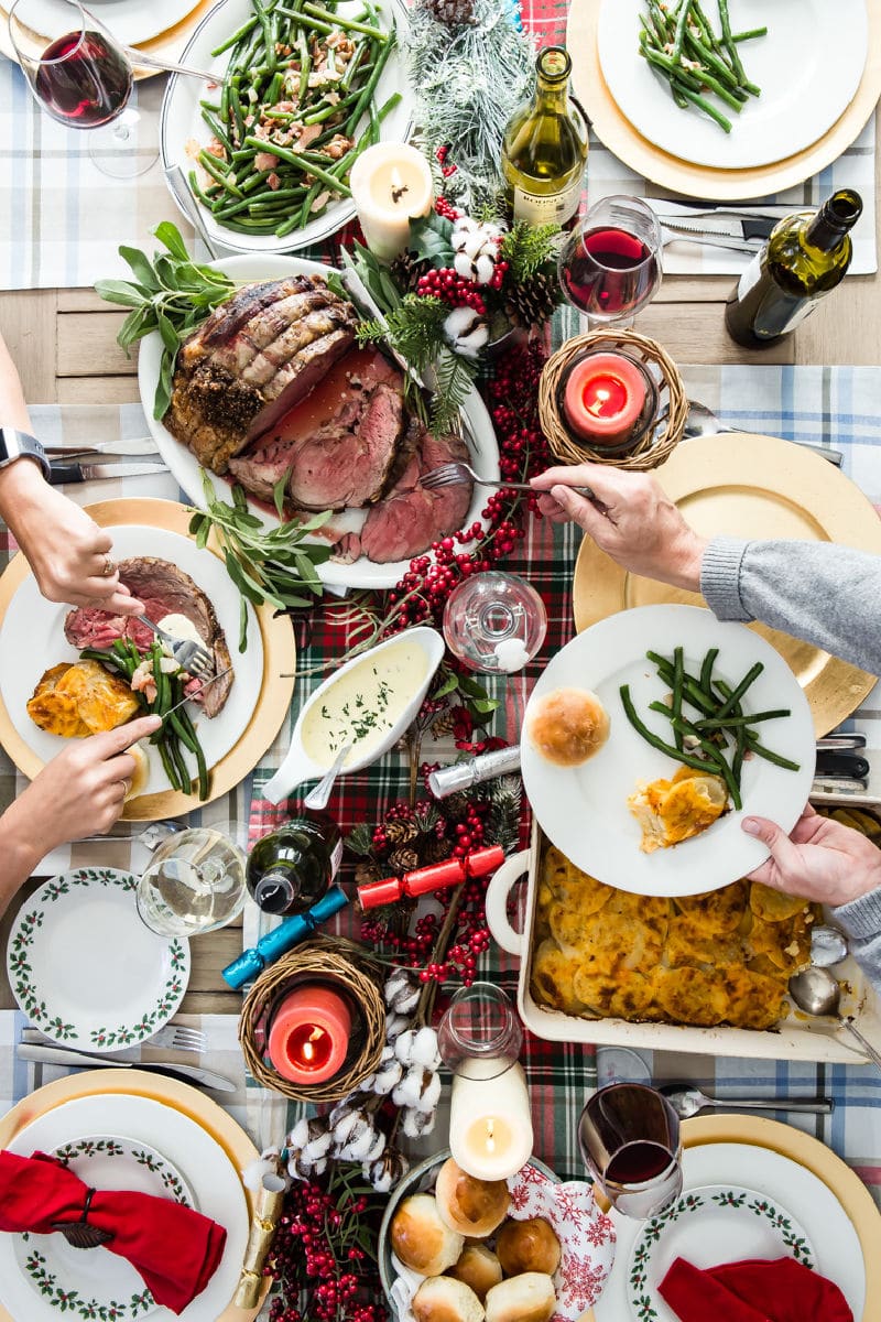 A Christmas table with prime rib, scalloped potatoes, green beans, and rolls.