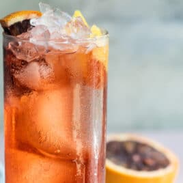 An Americano in a high ball glass with a blood orange garnish.