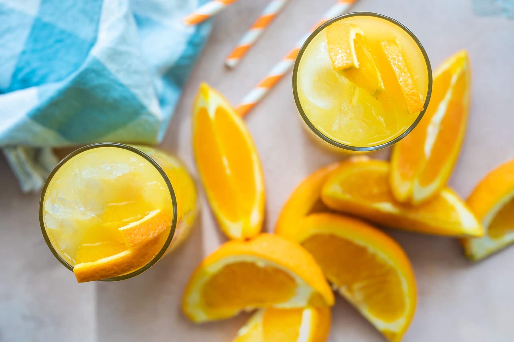 Two fuzzy navel cocktails surrounded by orange slices.