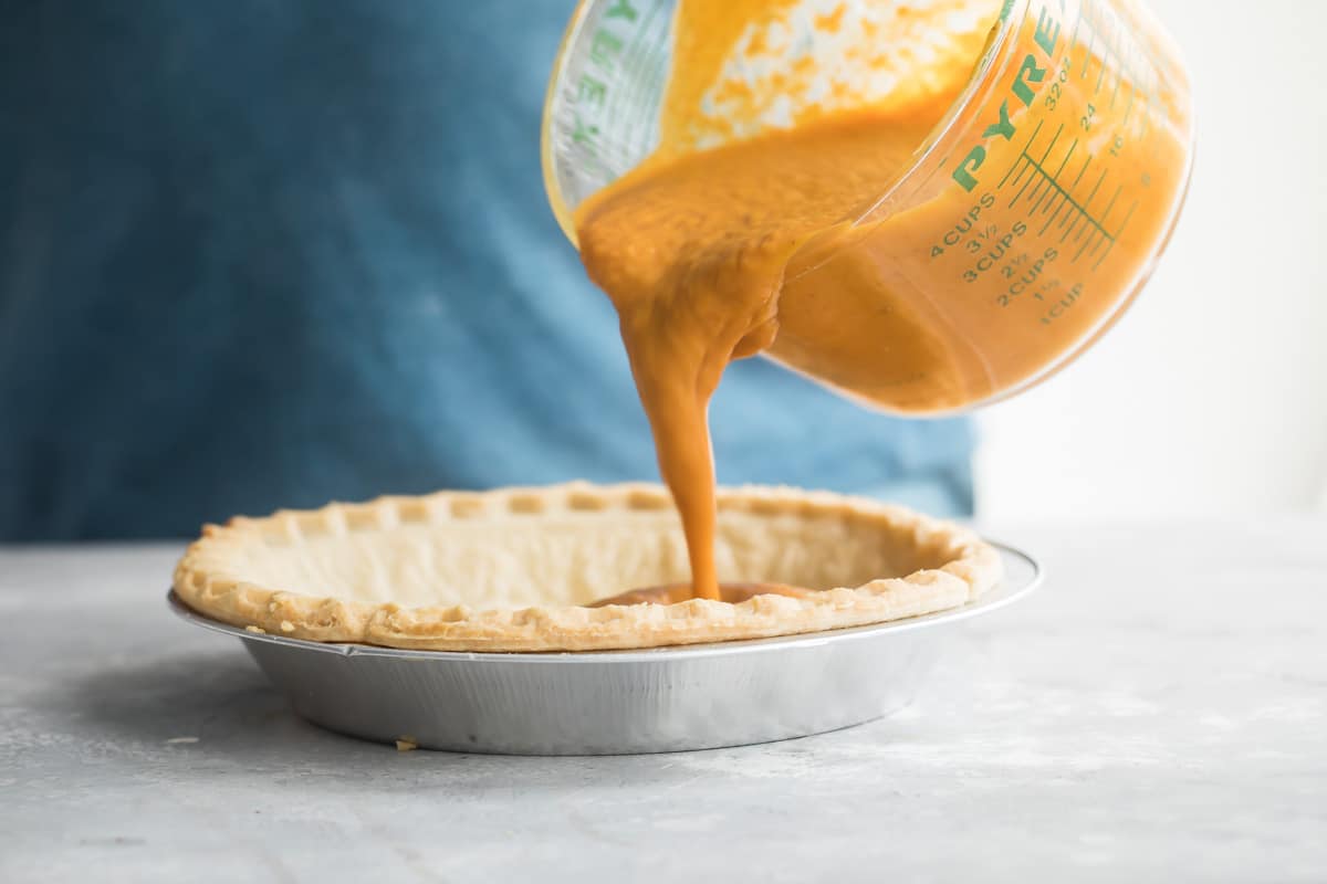 Pouring pumpkin pie filling in to a pie crust.